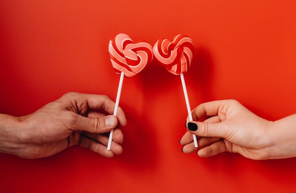 two hands bumping heart lollipops together